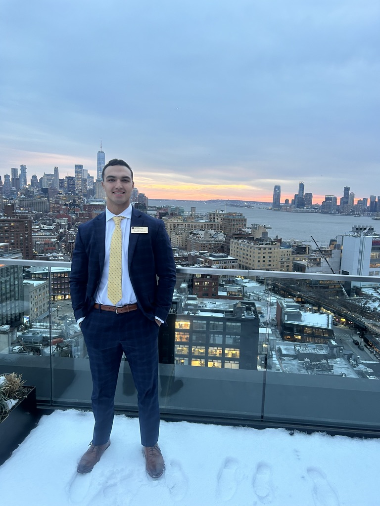 Randell in a suit on a New York City rooftop at sunset